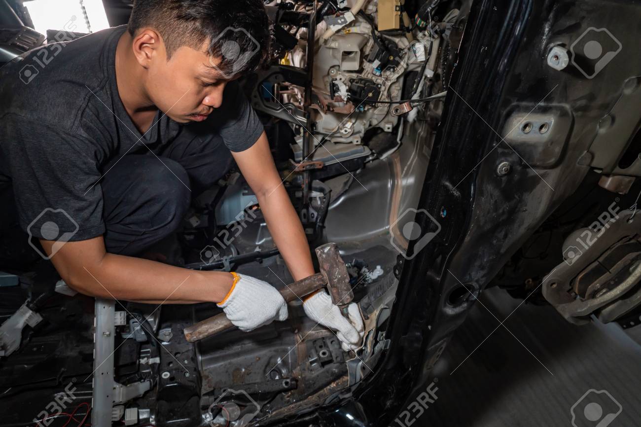 The repairer of the car body uses a hammer to break the damaged iron. ,Auto body repair series : Fixing car body